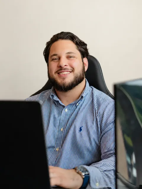 Portrait of JP Infante, Ethos co-founder who leads strategy and sales, smiling at his desk