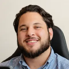 JP Infante, co-founder of Ethos Web Development & SEO, smiling at his desk in a striped shirt