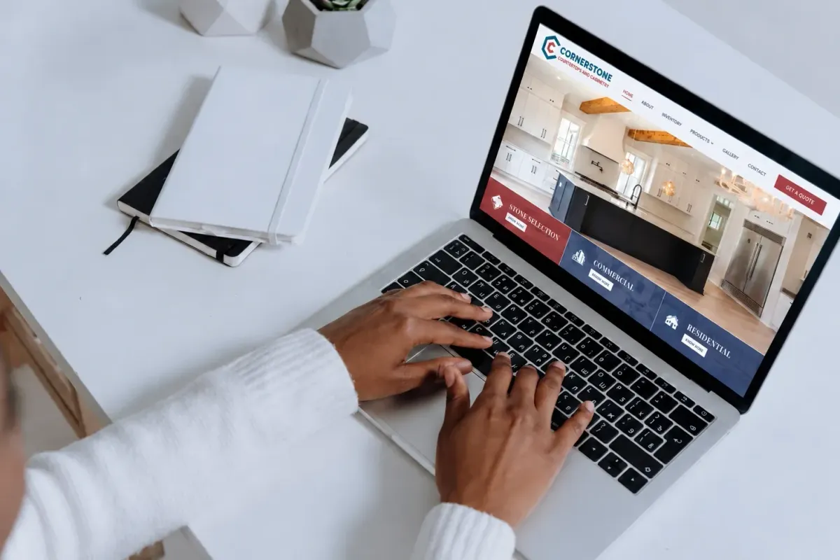 Hands typing on a laptop that shows the Cornerstone Countertops and Cabinetry website built by Ethos Web Development & SEO