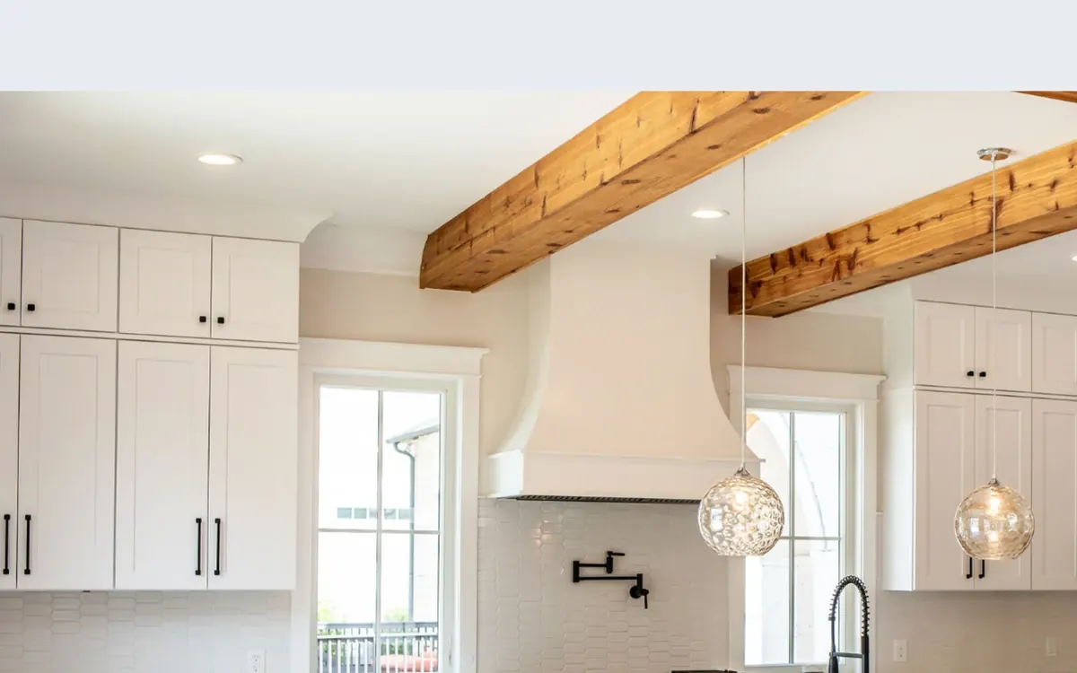 Finished kitchen with white cabinets, wood ceiling beams and pendant lights