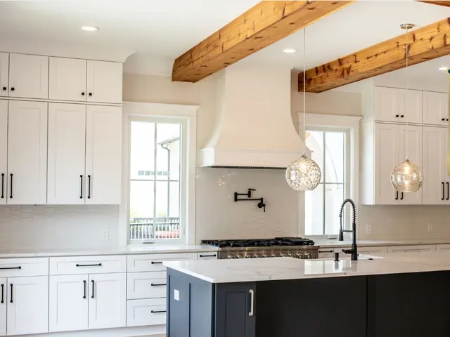 Bright kitchen with white shaker cabinets, a dark island and exposed wood beams